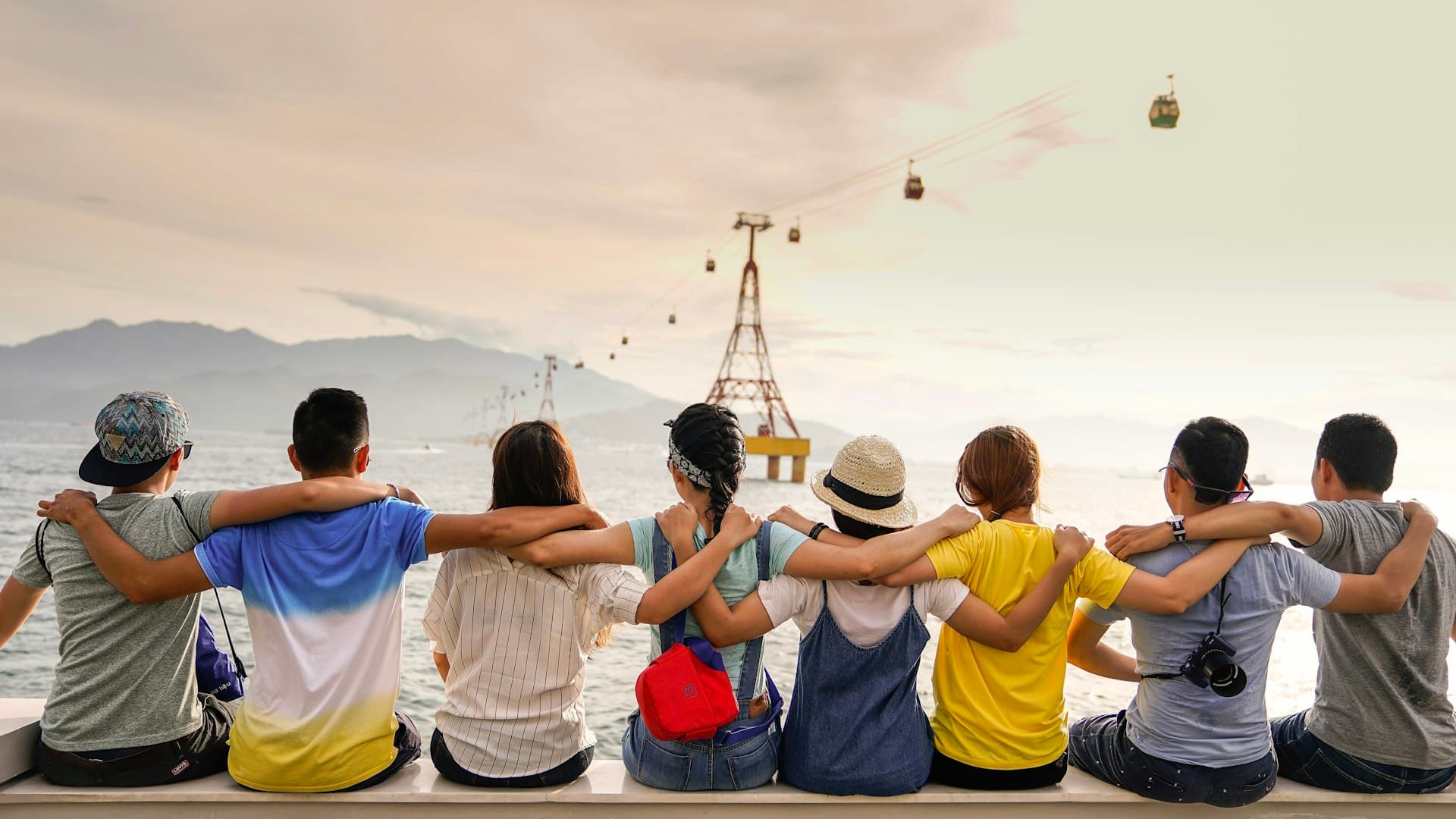 Friends sitting together with arms around each other, looking out at a sunset over water